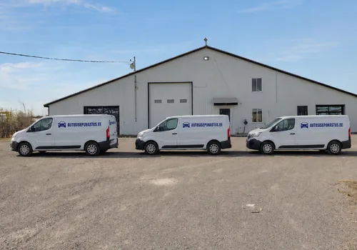 Päikesepaistel töökojahoone ees kolm valget autosisepuhastus.ee kirjaga kaubikut, halli rullukse kohal on õhkkardin, mis hoiab talvel külma õhu hallist väljas.