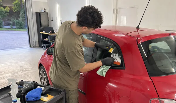 Kleebiste ja liimijääkide eemaldamine punase auto külgaknalt plastkaabitsaga, tagaklaasilt kleebise eemaldamise järel kontrollitakse, et kõik kütteniidid soojenevad.